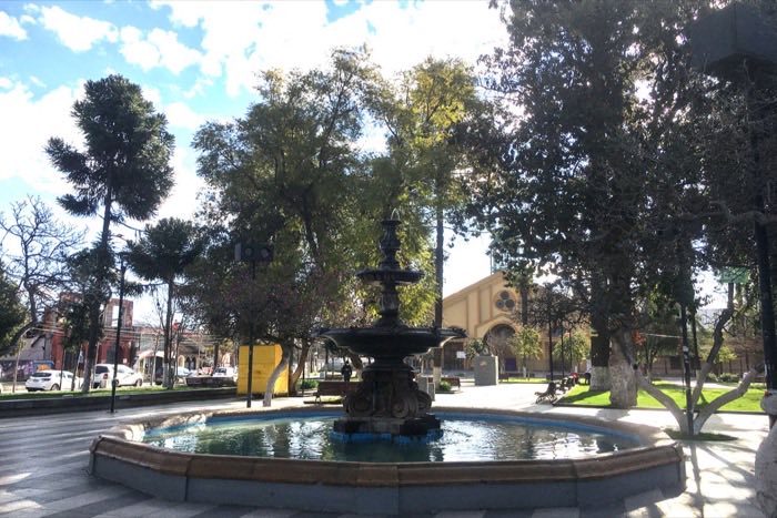 La pileta de piedra de la Plaza de Armas de Rengo en un día despejado, rodeada de árboles.