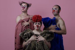 Los tres payasos de Festín de la Risa retratados sobre un fondo rosado, envueltos en abrigos de piel y con la nariz roja puesta.