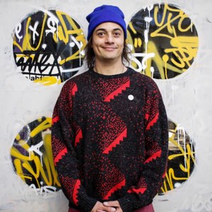 Felipe Godoy apoyado en un muro pintado, con gorro azul y un chaleco de lana negro y rojo.