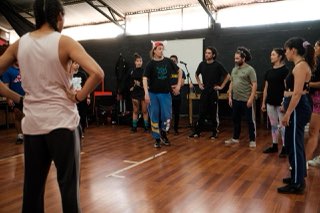 El profesor, con una gorra de orejas, muestra un movimiento en medio de la rueda de participantes.