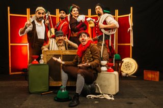 El elenco rodeado de baúles, instrumentos y objetos de circo.