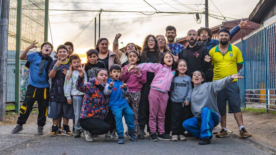 Grupo de niñas, niños y adultos de la comunidad reunidos en la calle al atardecer.